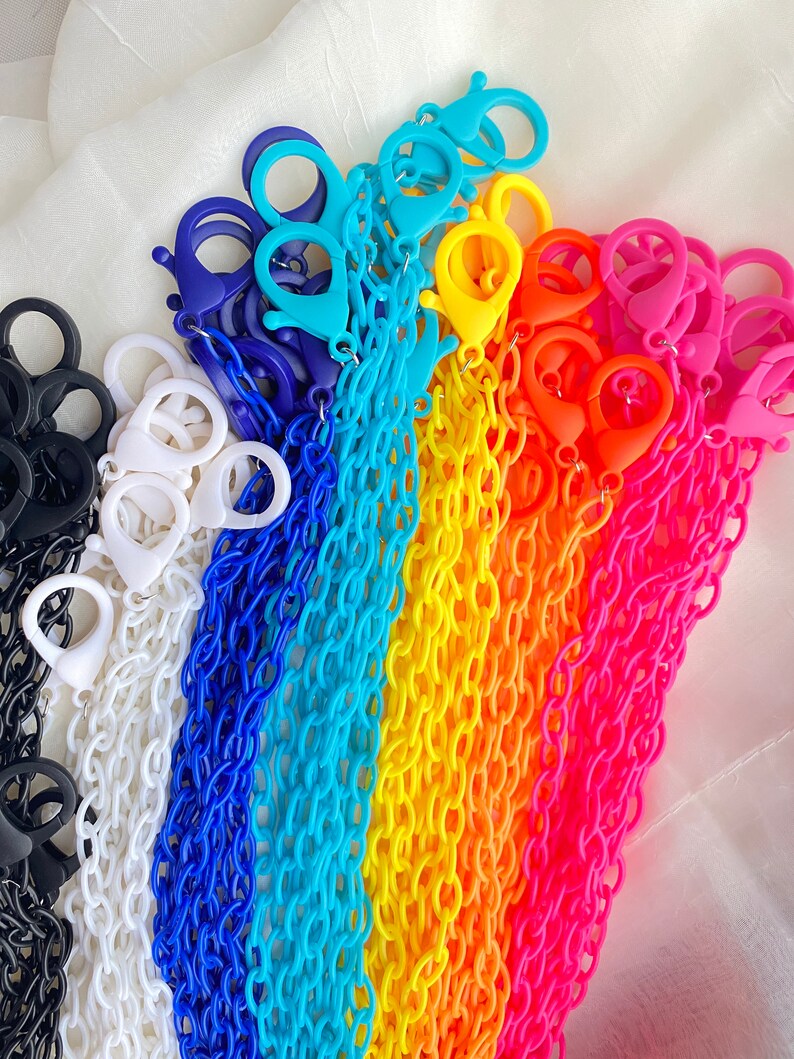 May include: A rainbow assortment of colorful plastic chains with lobster clasps. The chains are arranged in a rainbow pattern, starting with black, white, blue, light blue, yellow, orange, and pink.