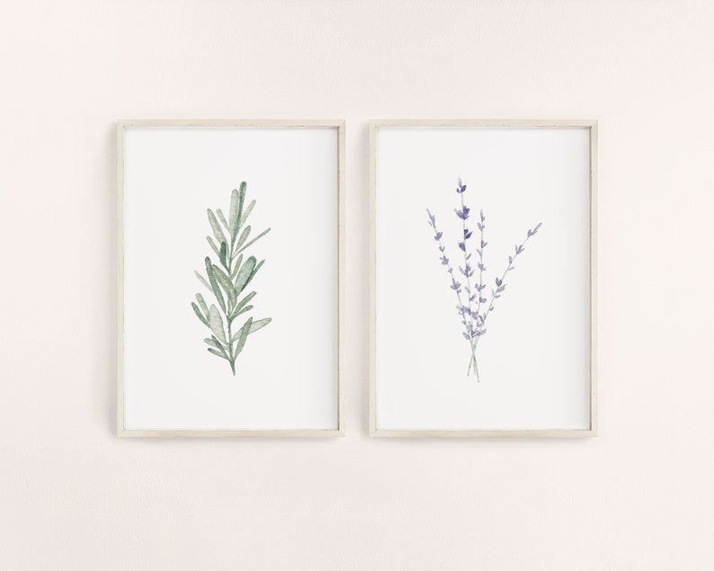 K&ouml;nnte beinhalten: Zwei gerahmte botanische Drucke. Einer zeigt einen Aquarellzweig gr&uuml;nen Rosmarins. Der andere Druck zeigt einen Aquarellstrau&szlig; lila Lavendel. Beide Drucke haben einen wei&szlig;en Hintergrund und sind in hellen Rahmen.