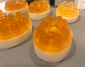 May include: Four round, white and orange soaps with a textured surface. The soaps are arranged in a row on a gray surface.