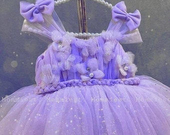 May include: A lavender tulle dress with a braided waistband and flower embellishments. The dress has a sparkly finish and is adorned with bows on the straps.