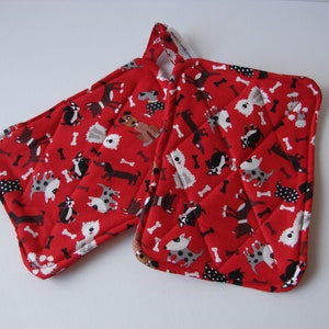 May include: A pair of red quilted pot holders with a pattern of black, white, and brown dogs and bone shapes.