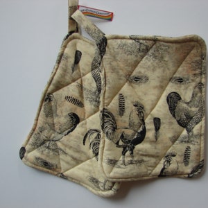 Puede incluir: Dos agarraderas de olla acolchadas de color beige con un estampado de gallo en blanco y negro. Las agarraderas tienen un lazo para colgar.