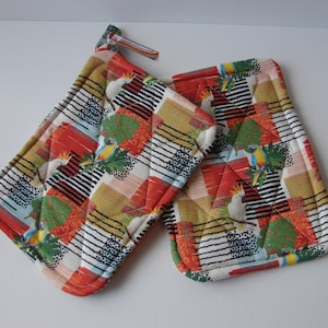 May include: A pair of red, white, and black quilted pot holders with a tropical bird print. The pot holders feature a design of parrots and cockatoos on a geometric background.