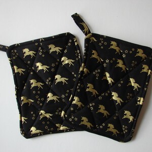 Puede incluir: Dos agarraderas negras acolchadas con un estampado dorado de unicornios y estrellas. Cada agarradera tiene un pequeño lazo para colgar. Las agarraderas son cuadradas y miden aproximadamente 20 cm por 20 cm.