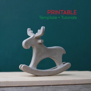 May include: A light gray, handmade rocking moose figurine. The moose has large antlers and is mounted on a curved base. The text "PRINTABLE Template + Tutorials" is in red and green above the moose.