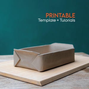 May include: A beige paper loaf pan rests on a light wood chopping board. The words "PRINTABLE Template + Tutorials" are in orange and white text above the pan. The background is a teal green colour.