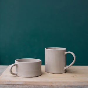 K&ouml;nnte beinhalten: Ein Set aus drei Keramikbechern mit gesprenkelter, matter Oberfl&auml;che. Die Becher sind in Creme-, Hellgrau- und Dunkelgraut&ouml;nen gehalten. Jeder Becher hat ein schlichtes, minimalistisches Design.