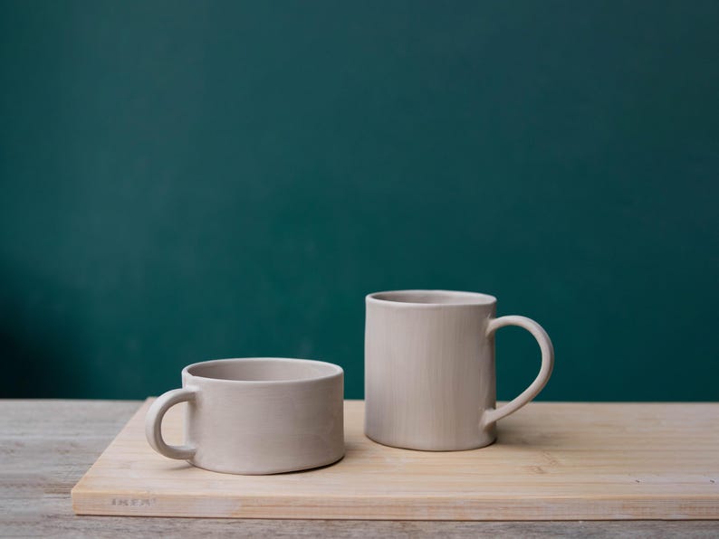K&ouml;nnte beinhalten: Ein Set aus drei Keramikbechern mit gesprenkelter, matter Oberfl&auml;che. Die Becher sind in Creme-, Hellgrau- und Dunkelgraut&ouml;nen gehalten. Jeder Becher hat ein schlichtes, minimalistisches Design.