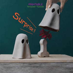 Könnte beinhalten: Eine skurrile Halloween-Szene mit drei Keramik-Geisterfiguren. Eine Geisterfigur steht aufrecht, eine andere wird gehalten, und die dritte ist eine Vase mit einer roten Blume. Das Wort "Surprise!!" ist orange geschrieben. Der Hintergrund ist dunkelblaugrün.