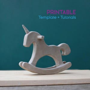 May include: A light gray, handcrafted rocking horse figurine with a unicorn horn. The toy is made of a matte material and sits on a wooden surface. The text "PRINTABLE Template + Tutorials" is in the background.