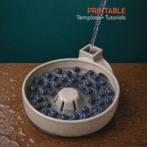 May include: A beige ceramic berry colander with a central drainage column and a side spout, filled with fresh blueberries being rinsed under a stream of water. The text PRINTABLE Template + Tutorials is visible in the upper right corner.