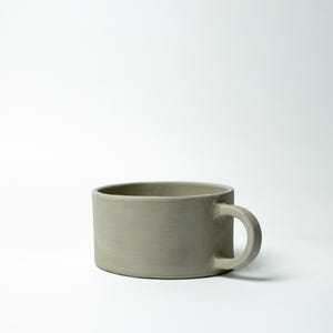 K&ouml;nnte beinhalten: Ein Set aus drei Keramikbechern mit gesprenkelter, matter Oberfl&auml;che. Die Becher sind in den Farben Creme, Hellgrau und Dunkelgrau gehalten. Jeder Becher hat ein schlichtes, modernes Design und einen abgerundeten Henkel.