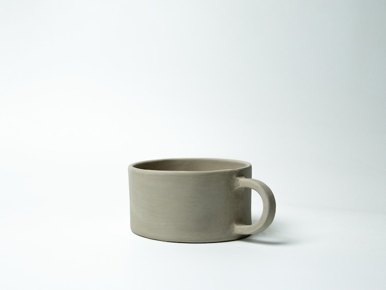 K&ouml;nnte beinhalten: Ein Set aus drei Keramikbechern mit gesprenkelter, matter Oberfl&auml;che. Die Becher sind in den Farben Creme, Hellgrau und Dunkelgrau gehalten. Jeder Becher hat ein schlichtes, modernes Design und einen abgerundeten Henkel.