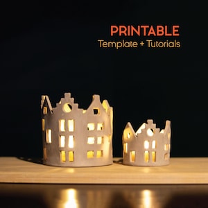 Puede incluir: Dos candelabros de cerámica con forma de casas, con ventanas y puertas recortadas, se encuentran sobre una superficie de madera. Los candelabros están iluminados desde dentro, proyectando un brillo cálido. El texto "PRINTABLE Template + Tutorials" está incluido.