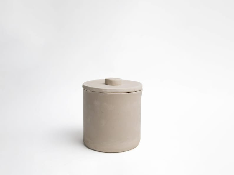K&ouml;nnte beinhalten: Ein zylindrischer, beigefarbener Keramikbeh&auml;lter mit passendem Deckel und kleinem Knauf. Der Beh&auml;lter hat ein schlichtes, minimalistisches Design, das sich f&uuml;r die Aufbewahrung oder Pr&auml;sentation eignet. Die neutrale Farbe und die klaren Linien verleihen ihm eine moderne &Auml;sthetik.