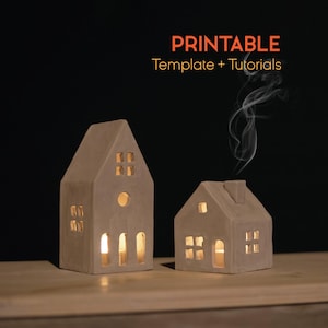 May include: Two beige ceramic house-shaped candle holders with lit candles inside, emitting a warm glow. One house is taller with a round window, the other is smaller with a chimney. The image includes the text "PRINTABLE Template + Tutorials".