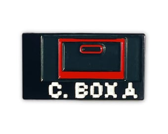 May include: Black and red enamel pin featuring a pixelated image of a video game cartridge and the text "C. BOX A".