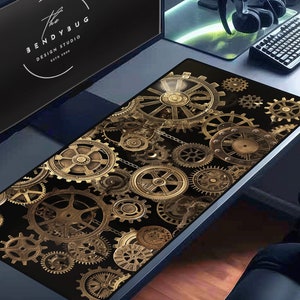 Puede incluir: Un ratón de ordenador negro y dorado con un diseño de engranajes entrelazados. El ratón está sobre un escritorio con un monitor de ordenador, un teclado y unos auriculares.