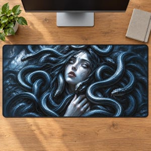 May include: A rectangular desk mat featuring a dark, monochromatic blue illustration of a person with closed eyes surrounded by numerous intertwined snakes. The detailed artwork covers the entire surface of the mat, showcasing a complex composition of scales and human features in a cool, moody colour palette.