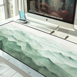 May include: A green and white desk mat with a watercolor design of mountains and clouds. The mat is on a white desk with a computer and keyboard.