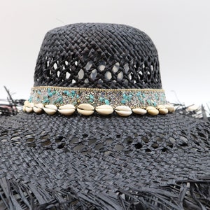May include: A wide-brimmed black straw hat with a decorative band of turquoise and white beads and seashells.