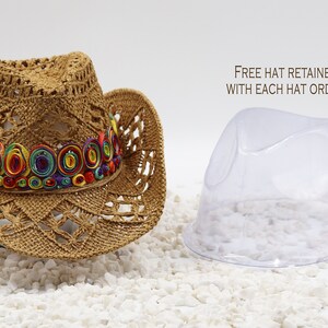 May include: A brown crocheted cowboy hat with a colorful, multi-layered ribbon band. The hat is sitting on a white surface.  Free hat retainer with each hat order.