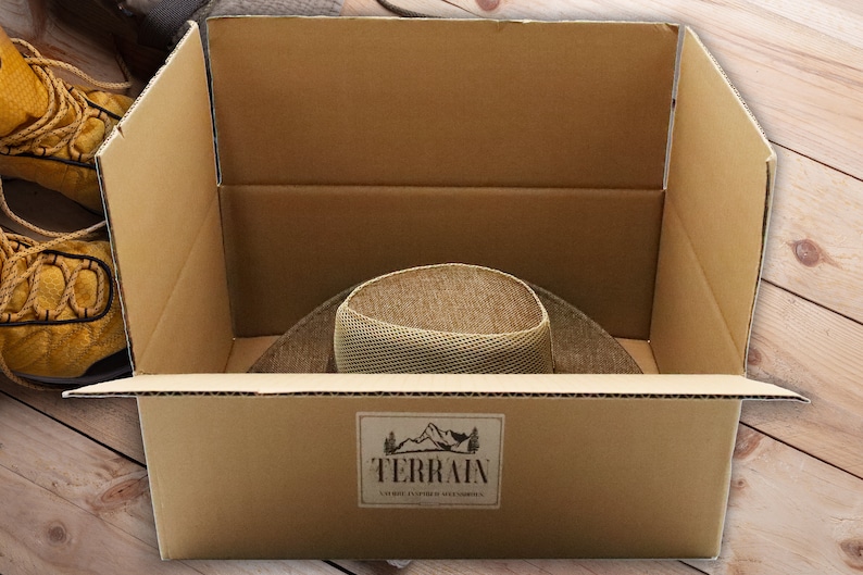 May include: A brown cardboard box with the word "TERRAIN" printed on the side. The box is open and a brown hat is inside.