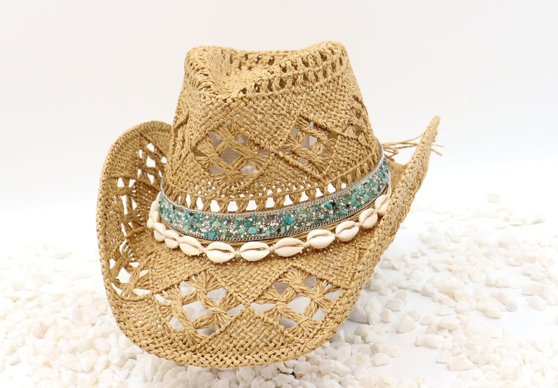 May include: A straw cowboy hat with a turquoise and silver beaded band and a row of white seashells.