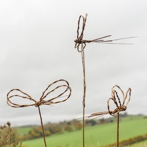 May include: Three brown twig dragonfly sculptures with wire wings against a cloudy sky background.