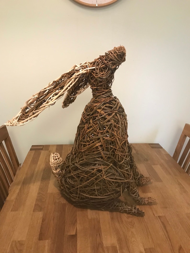 May include: A brown and white woven willow sculpture of a rabbit sitting on a wooden table.