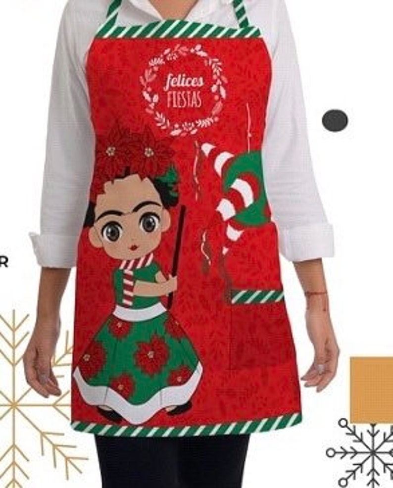 Puede incluir: Delantal rojo de Navidad con borde de rayas verdes y blancas. El delantal presenta una ilustraci&oacute;n de dibujos animados de Frida Kahlo con un vestido verde y una corona de flores rojas. El texto "felices fiestas" est&aacute; escrito en una corona sobre su cabeza.