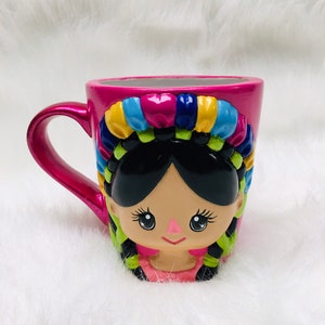 Puede incluir: Una taza de cerámica con un diseño vibrante. La taza es principalmente rosa intenso con un asa y una ilustración detallada de una niña con trenzas negras y tocado colorido. El diseño presenta colores brillantes como amarillo, azul y verde.
