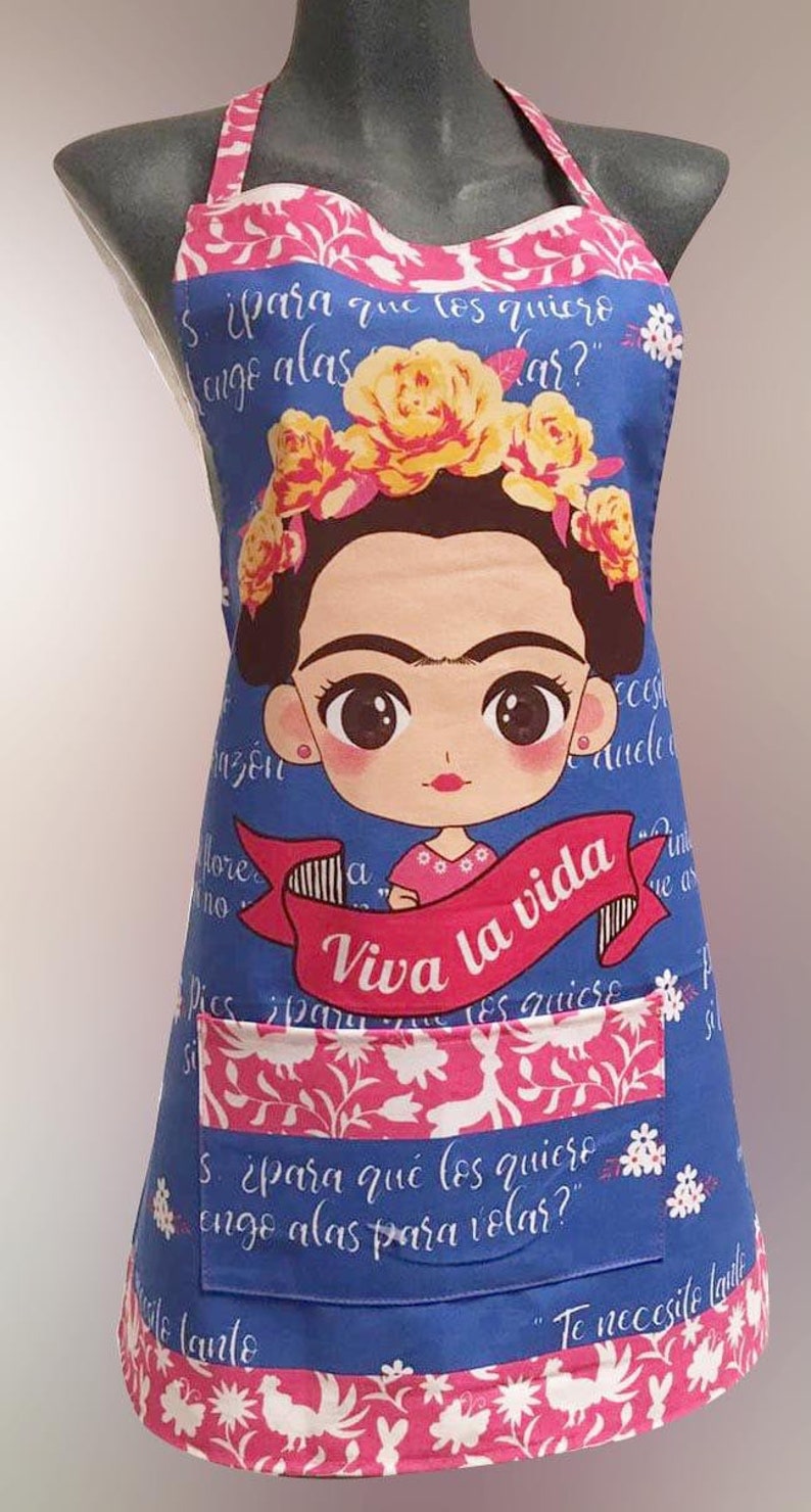 Puede incluir: Un delantal azul con una ilustraci&oacute;n colorida de Frida Kahlo. El delantal tiene un bolsillo grande con el texto "Viva la vida" y la frase "&iquest;para qu&eacute; los quiero, engo alas para volar?" en espa&ntilde;ol.