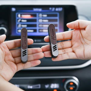 May include: Two wooden car air fresheners with metal accents. The air fresheners are engraved with the names "Carmichael" and "Harrison".