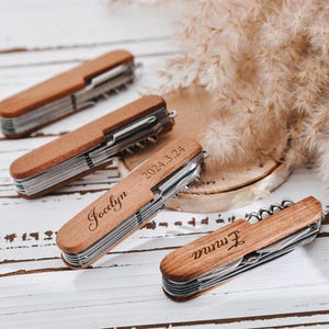 May include: Four wooden pocket knives with personalized engravings. The knives have a silver blade and a wooden handle. The engravings include names and a date.
