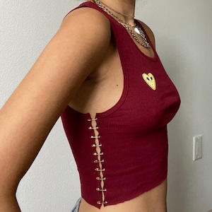 May include: A maroon tank top with a yellow heart design and a row of safety pins down the side seam.