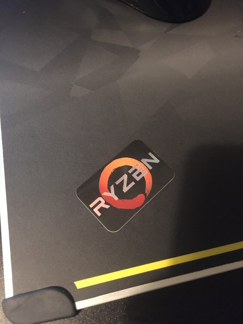 May include: A black and red sticker with the word "RYZEN" in white letters. The sticker has a circular design with a red and orange gradient.