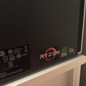 May include: A black computer case with a Ryzen 5 sticker and a Windows sticker. The case has a textured surface and a vent on the right side.