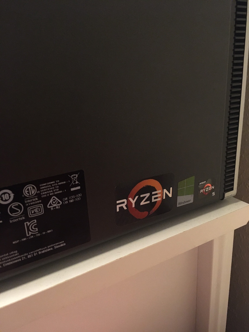 May include: A black computer case with a Ryzen 5 sticker and a Windows sticker. The case has a textured surface and a vent on the right side.