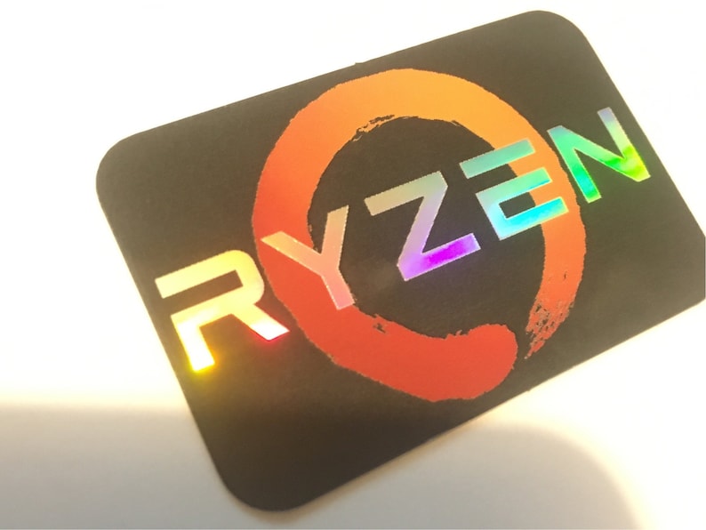 May include: A black sticker with a holographic, rainbow-colored "RYZEN" logo. The logo is surrounded by a red circle with a brushstroke design.
