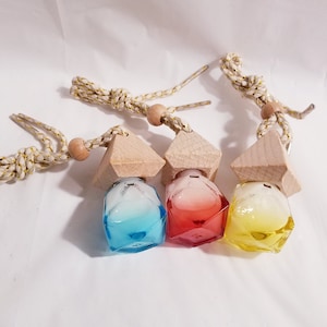 Puede incluir: Tres ambientadores para coche coloridos. Cada uno tiene una botella de vidrio geométrica en azul, rojo y amarillo, coronada con una pirámide de madera y una cuerda beige y dorada. Diseñado para colgar en un vehículo.