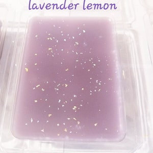 May include: A rectangular, lavender-colored wax melt with gold flecks, presented in a clear plastic container. The text "lavender lemon" is written in a purple script at the top. The wax melt is a solid, smooth block.
