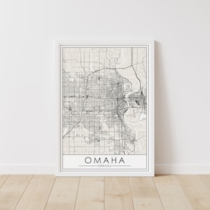 Puede incluir: Una impresión de mapa en blanco y negro de Omaha, Nebraska. El mapa muestra las calles de la ciudad y los principales puntos de referencia. El nombre de la ciudad está impreso en negro con fuente sans-serif en la parte inferior del mapa.