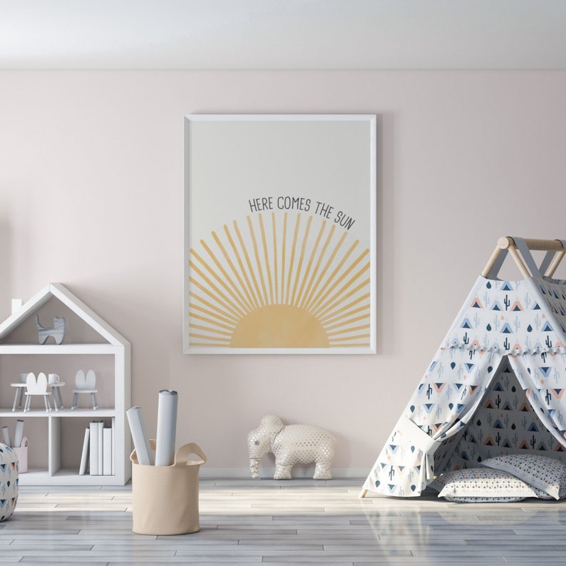 May include: A white framed print with a yellow sun and the text "Here comes the sun" in a children's playroom. There is a white toy elephant, a white bookshelf with toys, and a blue and white patterned teepee tent.