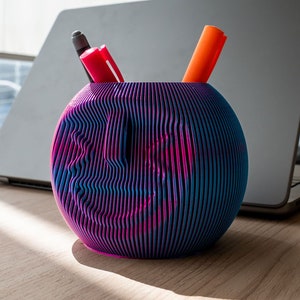 May include: A blue and pink striped sphere shaped desk organiser with a red and orange pen inside.