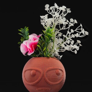 May include: A terracotta vase with a textured, infinity symbol design holds a bouquet of pink and white flowers. The vase is round and has a smooth, glossy finish.