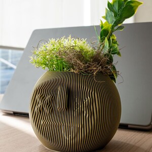 May include: A gold-coloured, round, textured ceramic planter with a variety of green plants inside. The planter has a wavy, ribbed design.