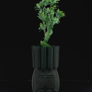 May include: A dark green ceramic vase with a textured surface and a small green plant growing inside.