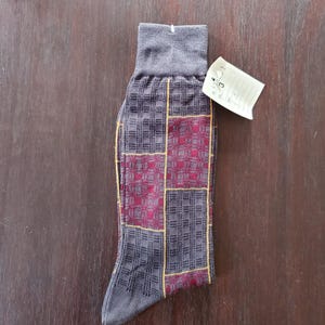 May include: A single gray sock with a patchwork design featuring burgundy and gray squares outlined in yellow. The sock has a ribbed cuff and a small tag attached.