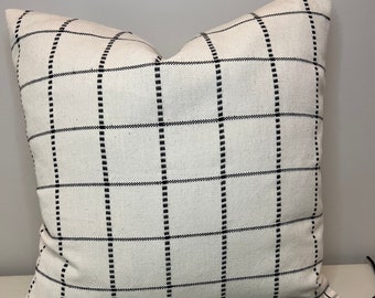 May include: White pillow with black grid pattern. The pillow is on a white surface with black eucalyptus leaves.